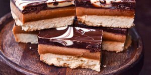 Chocolate and caramel topped shortbread biscuit on a wooden board