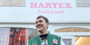 A young man in a green baseball jacket stands in front of a shop