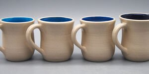 Four ceramic mugs in a row with beige outsides, and glazed blue interiors