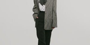 Image of a woman wearing a scarf and a grey blazer with black trousers.