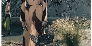 Image of a woman standing in the desert wearing a black and brown dress.