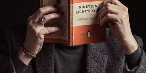 Image of a man holding a book in front of his face.