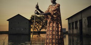 Image of a woman stood in a lake holding a stick.