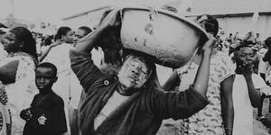 A black and white image of a woman carrying a basket on her head.