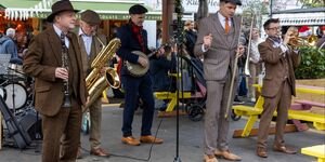 A group of four men stand under a bandstand holding instruments. All are dressed in brown suits