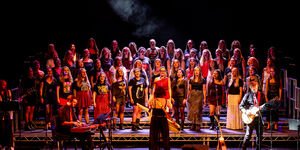 Photograph of a large female choir, all members are standing and singing