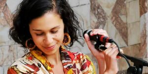 A young women wearing an orange and yellow patterened blouse stands in front of a microphone