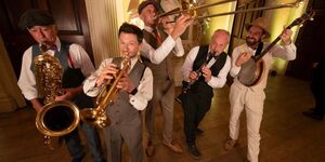 A photo of 5 musicians in suits playing various instruments including brass