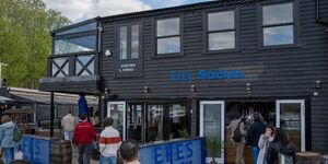 The outside of a wooden-clad bar with people walking around outside of it