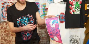 A man holding up a t-shirt with an illustration design on it.