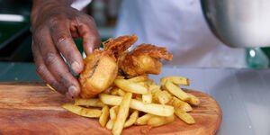 A person puts vegan 'fish' and chips onto a wooden board. Only their hand is visible