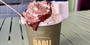 A close-up of a hot chocolate topped with whipped cream, in a green paper cup