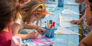 A group of children sit at a table colouring in bunting