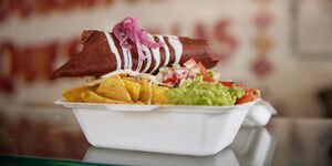 A white food container filled with tortilla chips and guacamole