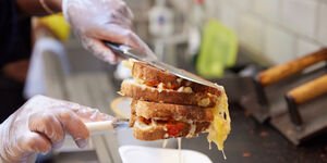 A toasted cheese sandwich is held between two metal cooking tools
