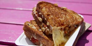 A toasted cheese sandwich in a white carton on a pink picnic bench