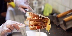 A toasted sandwich with cheese oozing out is held above a stove