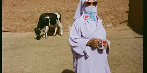 Image of a woman in a headscarf stood in front of a cow.