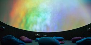 Rainbow colours projected on a screen in a room with cushions.