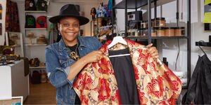 A woman stands smiling, holding a red & gold cape on a hanger