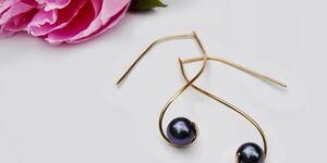 An image of a pair of earrings with a pink rose in the background.