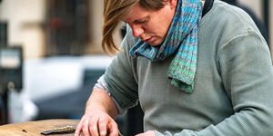 A man wearing a green jumper and scarf sits with a guitar on his lap