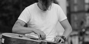 A black an white photo of a young man with his head down, looking at a guitar flat on his lap