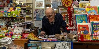 Image of an elderly man standing behind the counter in a corner shop.