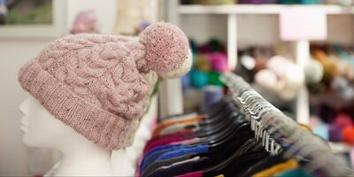 A pink hat is displayed on a white head. In the background are rails of clothes.
