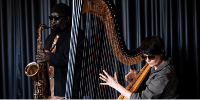 A woman sits at a harp whilst a man stands playing the sxophone