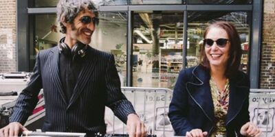 A man and a woman stand smiling in front of some turntables
