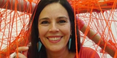 A woman with dark brown hair smiles at the camera. In the background are hanging threads of red string