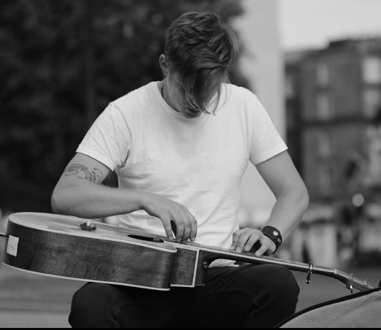 A black and white photograph of a man looking down at a guitar on his lap